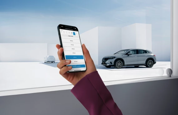 Nahaufnahme eines Smartphones mit Buchungs-App, im Hintergrund ein silberner Mercedes-Benz EQS SUV und ein weißes Auto in modernem Setting.